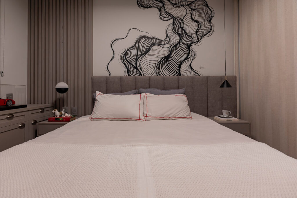 No caso deste quarto, a opção foi por uma ambientação leve, com tons de cinza e destaque para a obra de arte ao fundo da cabeceira. Mesmo com o quadro sendo branco e preto - cores também consideradas mais clássicas, os contornos do desenho roubam completamente a atenção. / Projeto de apartamento da arquiteta Luana Ogata e foto de Emerson Rodrigues